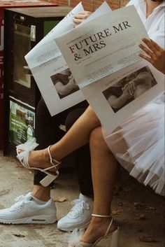 two people sitting on a bench with newspapers in their hands and one person wearing white shoes