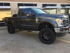 a black truck parked in front of a building with large tires on it's tires