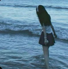 a woman standing in the ocean with her back to the camera and looking into the water