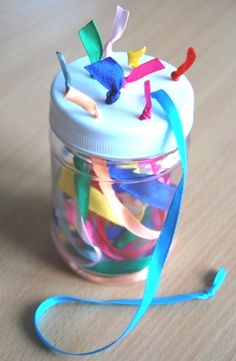 a glass jar filled with colorful streamers on top of a wooden table next to a blue ribbon