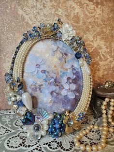 an ornate photo frame with pearls, beads and other items on a lace tablecloth