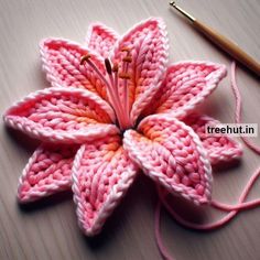 a crocheted pink flower sitting on top of a table next to a knitting needle