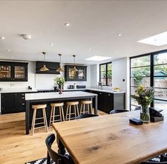 an open kitchen and dining area with wooden table, bar stools and black cabinets