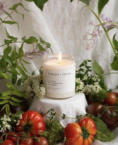 a candle sitting on top of a white cloth surrounded by tomatoes and other vegetables next to flowers