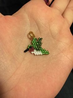 a person's hand holding a small green and white beaded bird charm