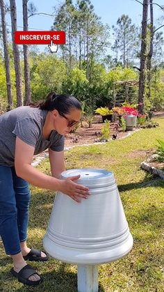 a woman placing a large white bell on top of a table in the grass next to trees