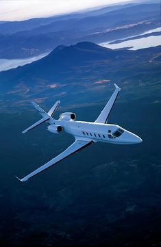 an airplane flying in the sky over some mountains and water, with one wing extended