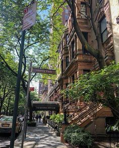 an apartment building on the corner of a street with trees and people walking down it