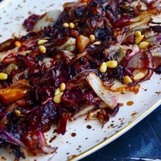 a white plate topped with red cabbage covered in nuts and seasoning next to a fork