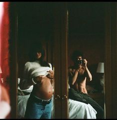 a man taking a selfie in front of a mirror with his pregnant belly exposed