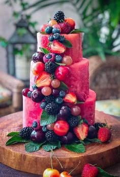 a watermelon cake with berries and cherries on the top is sitting on a wooden platter