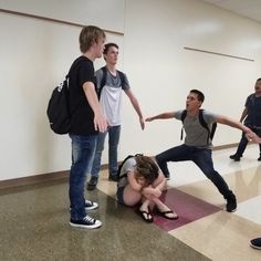 a group of young men and women standing around each other in a room with one woman laying on the floor