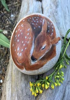 a rock with a deer painted on it sitting next to some yellow flowers and grass