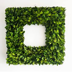 a square shaped boxwood wreath is hanging on a white wall, with the letter d surrounded by green leaves