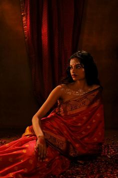 a woman is sitting on the floor in a red and gold sari with her eyes closed