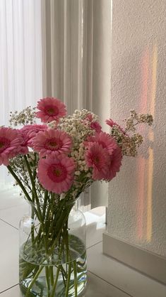 a vase filled with pink and white flowers sitting on top of a table next to a window