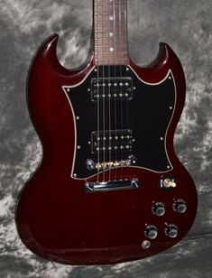 a red electric guitar sitting on top of a gray background