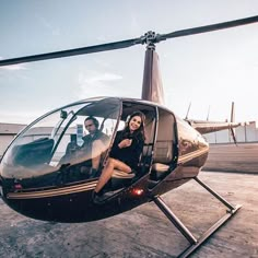 a man and woman sitting in the cockpit of a helicopter on an airport tarmac