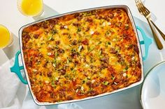 a casserole dish with meat and vegetables in it next to two glasses of orange juice