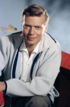 a man sitting on top of a red chair wearing a white shirt and black tie