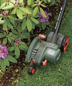 a green lawn mower sitting in the grass next to purple flowers