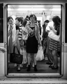 black and white photograph of people standing on subway platform with bags in front of them