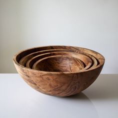 four wooden bowls stacked on top of each other in front of a white wall and floor