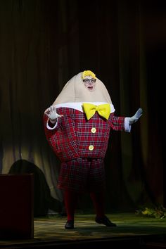 a man in a costume on stage with his arms out to the side, wearing glasses and a yellow bow tie