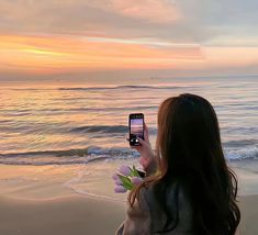 a woman taking a photo with her cell phone on the beach at sunset or sunrise