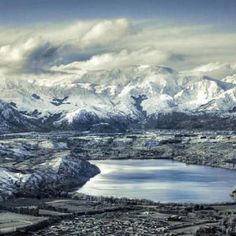 an aerial view of snow covered mountains and lakes in the foreground, with a city below