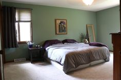 a bedroom with green walls and carpeted flooring has a large bed in the corner