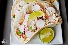 two tacos with radishes and limes on a plate