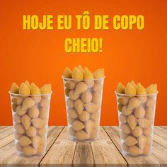 three plastic cups filled with potatoes sitting on top of a wooden table next to an orange background