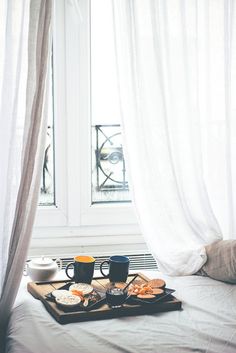 a tray with breakfast food on top of a bed next to two cups of coffee