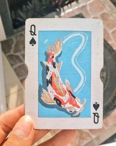 a hand holding up a playing card with a koi fish on it's back