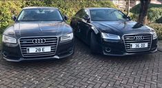 two black cars parked next to each other on a brick road in front of bushes