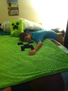 a young boy laying on top of a bed covered in a green minecraft blanket