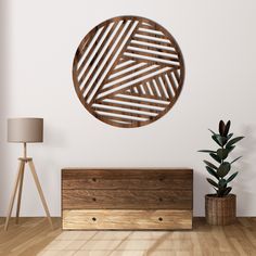 a round wooden wall decoration on a white wall next to a chest of drawers and a potted plant