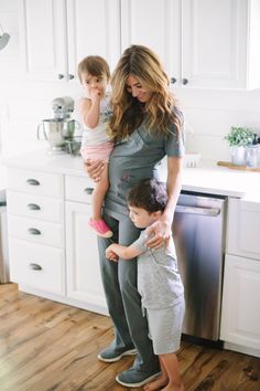 a woman holding two children in her arms while standing next to a stove top oven