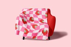 a red chair covered in a pink checkered blanket with strawberries printed on it