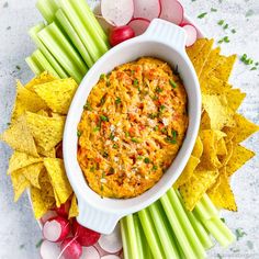 a white bowl filled with dip surrounded by celery, radishes and chips