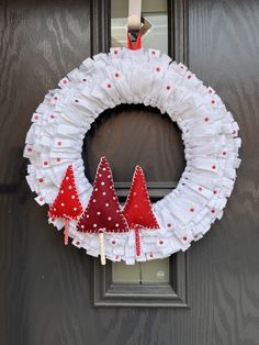 a white wreath with red trees hanging from it's side on the front door