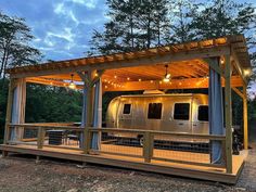 an rv is parked under a covered area in the woods at night with lights on