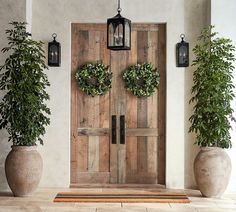 two potted plants sit in front of a wooden door with three wreaths on it