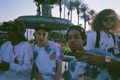 four young men sitting next to each other in front of a fountain and palm trees