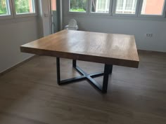 a wooden table sitting on top of a hard wood floor next to two large windows