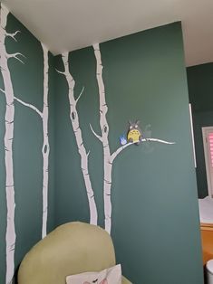 a bedroom with green walls and white trees painted on the wall, along with a yellow chair