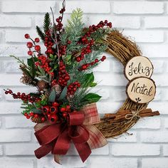 a christmas wreath with red berries and greenery hanging on a brick wall next to a wooden sign