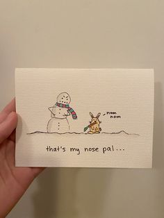 a hand holding up a card with a drawing of a snowman and a dog on it