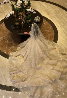 a woman in a wedding dress and veil is sitting on the floor next to a vase with flowers